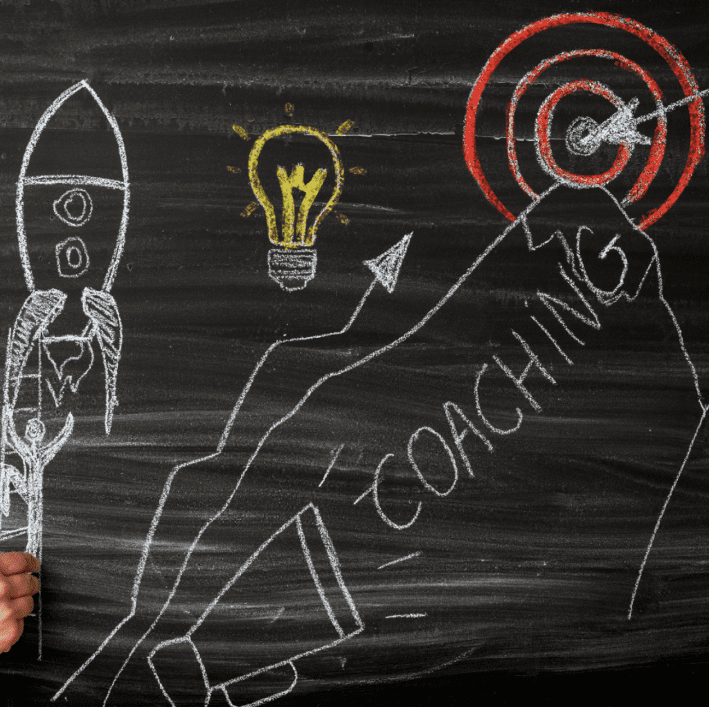 Business coaching training | Blackboard with drawings of rocketship, lightbulb and shooting target. The word 'coaching' is written out, coming out of a megaphone.